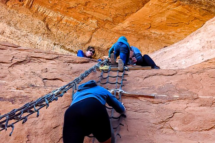 a couple of people that are climbing a rope ladder on the desert rocks
